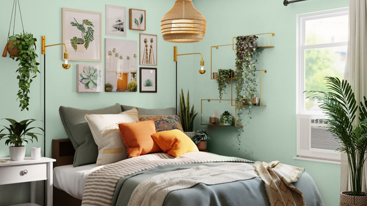 light green coloured bedroom with a neutral ceiling, with seven botanical artworks placed on the main wall, surrounded by leafy plants and a grey and white queen sized bed with grey and bright orange cushions