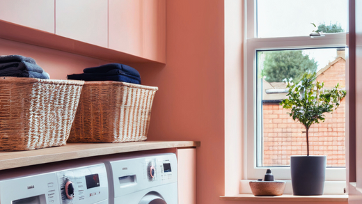 small utility room painted in a warm peach colour, with two big washing machines, grey carpet and wicker baskets