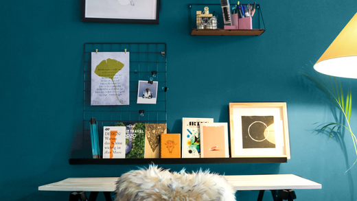 home office interior setting with a wooden desk with metal legs, white chair with a faux sheep skin throw, gallery wall and dark teal painted wall behind the furniture