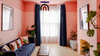 A cozy living room with coral pink walls, navy blue curtains, a dark blue sofa with patterned pillows, and indoor plants.