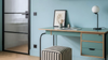 A modern teal and light wood writing desk with a matching striped upholstered stool, set against a light blue wall in a styled room.